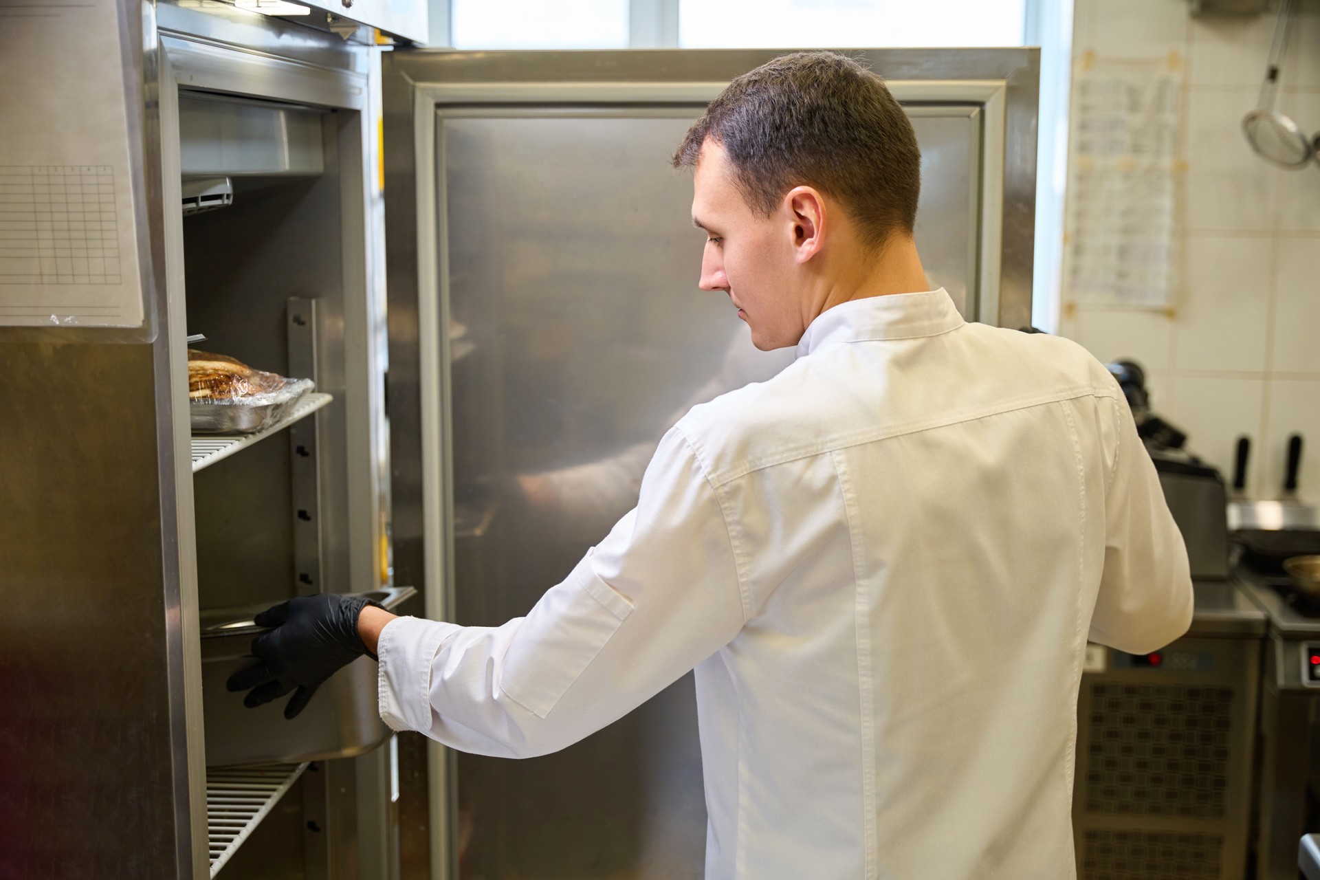Cook wearing protective gloves puts container of food in refrigerator